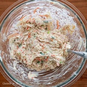 A fork mixing cream cheese, crab meat, green onions, and spices together in a large glass bowl.