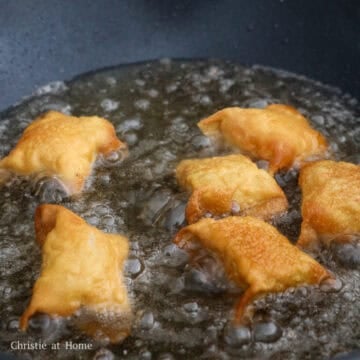 Several golden brown, blistered crab rangoons frying in a large pan of hot cooking oil.