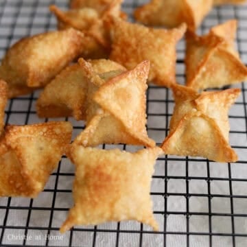 A slotted spoon transferring fried crab rangoons from hot oil onto a wire cooling rack.