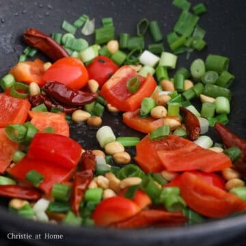 Dried red chilis, sliced green onions, peanuts, and red bell pepper pieces cooking together.