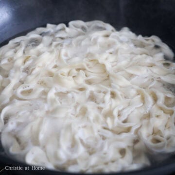 Noodles boiling in a pot of water and then being drained just before fully tender.