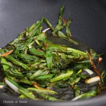 Scallions frying in hot oil in a pan until golden and lightly crisped at the edges.