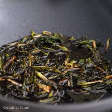 Sauce being poured into the pan with scallions and stirred to combine evenly.