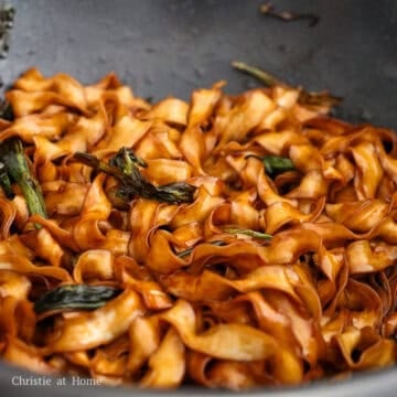 Cooked noodles being added to the pan and tossed until fully coated in the scallion oil sauce.