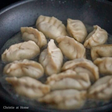 Next heat 1 tablespoon or 15 ml vegetable oil in a large non-stick pan on medium heat. Place dumplings flat bottom side down. Fry dumplings in small batches, about 12-14 pieces per batch. Pour just enough cold water to cover the base of the pan.