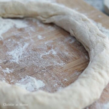 Evenly flour a clean working surface and transfer the kneaded dough ball on it. Then pierce a hole into the middle of the dough ball. Then shape it into a very loose circular "hoop". The hoop should be 1.5 inches thick.