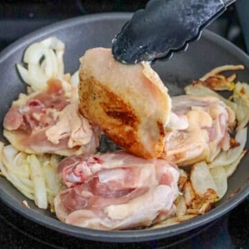 Chicken thighs searing skin-side down with softened onions.