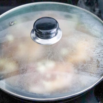 Chicken thighs simmering in adobo sauce with peppercorns and bay leaves.