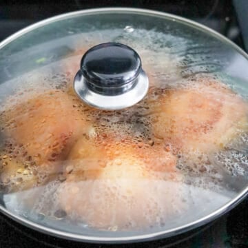 Chicken thighs flipped skin-side up in simmering adobo sauce.