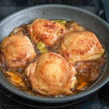 Cooked chicken thighs coated in thickened adobo sauce with softened onions.