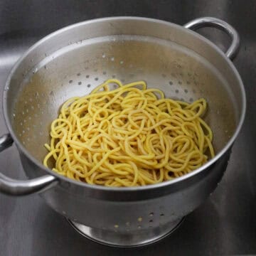 Pouring hot boiling water over noodles in a large bowl to loosen them up before draining.