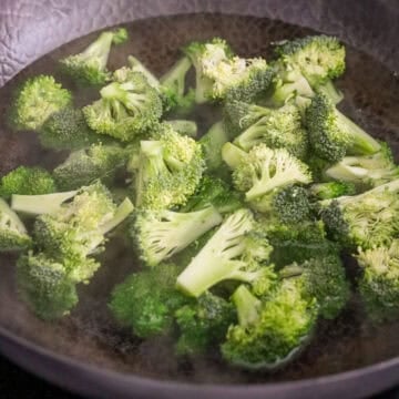 Bright green broccoli florets boiling rapidly in a large pan of hot water on the stovetop.