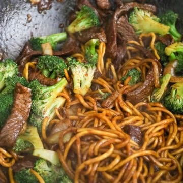 Tossing the stir-fried beef, noodles, translucent onions, and vibrant broccoli florets together with a glossy brown sauce in a large pan.