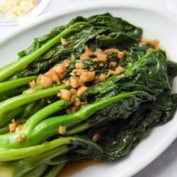 Cooked Chinese broccoli plated with garlic and savory sauce poured over top.