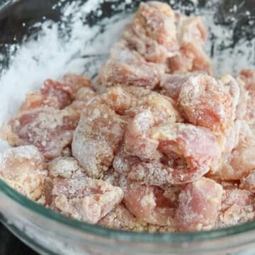 Tossing chicken pieces in cornstarch until evenly coated using tongs