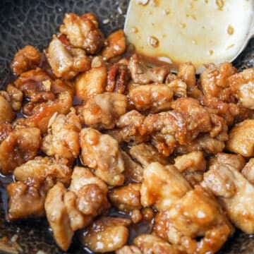 Tossing crispy chicken in thickened sauce until fully coated and garnishing with sesame seeds or lemon slices