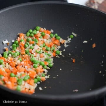 Minced garlic, diced shallots, orange carrots, and green peas sizzling together.