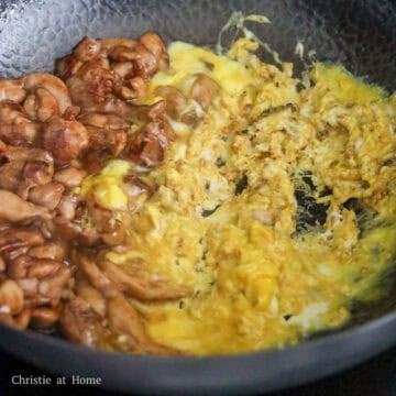 Chicken pieces and scrambled eggs searing together on one side of a large flat pan.