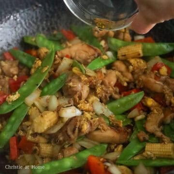 Diced onions, minced garlic, red bell pepper strips, green snap peas, and baby corn stir-frying together.
