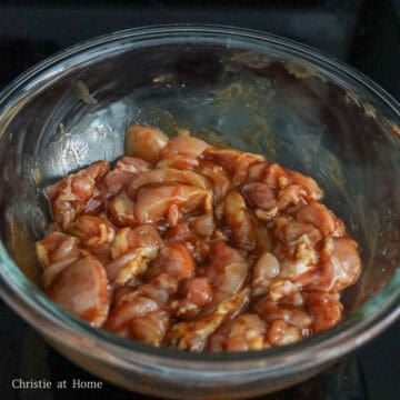 Sliced chicken mixed with savory dark marinade resting in a glass bowl.