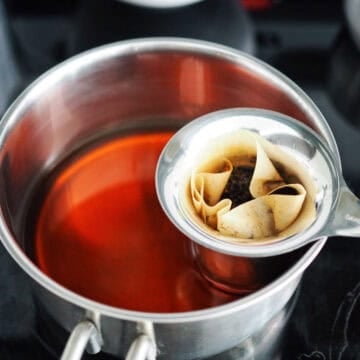 First in a tea strainer, line it with a coffee filter to help strain out very tiny tea leaves. Do not skip. Then fill the lined tea strainer with the tea leaves. If you're using black tea bags, you can skip this step and place the bags into the small pot. Then place the strainer into the small pot and fill the pot with 2 cups of water. Bring it a boil on medium-high heat. Reduce to low-medium heat to simmer and let this steep until it's very dark brown, about 5 minutes.