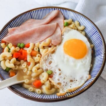 Bowls of pasta topped with ham slices and a fried egg, with hot broth being poured over before serving.