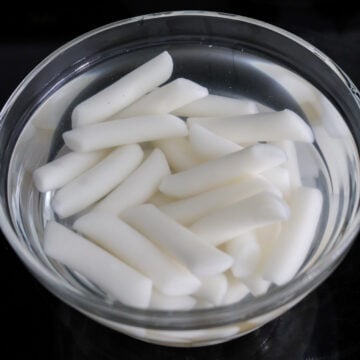 Rice cakes soaking in a bowl of warm water to soften before cooking.