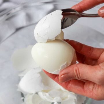 Soft-boiled egg being peeled with a spoon.