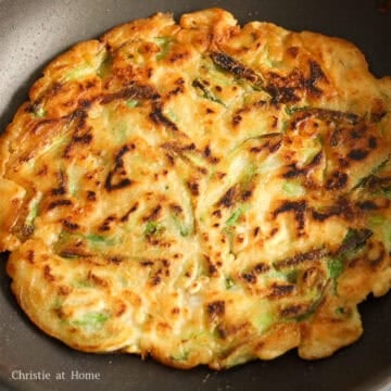 Flipping a golden brown crispy scallion pancake in a nonstick pan.