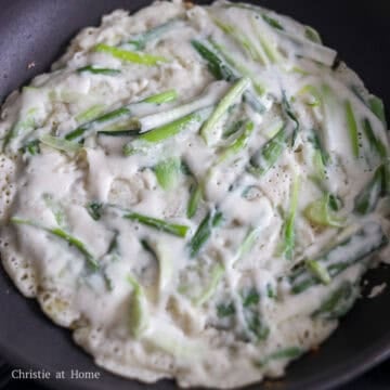 A thin layer of green onions and batter frying in a hot well oiled skillet.
