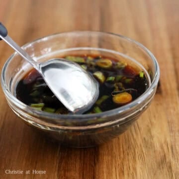 A small bowl of dark dipping sauce placed next to a plate of sliced crispy scallion pancakes.