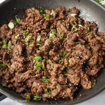 Cooked bulgogi beef topped with sliced green onions and white sesame seeds.