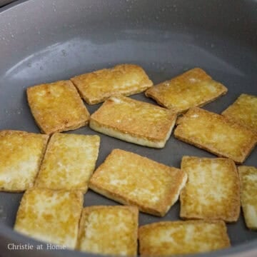 Tofu slices frying in a single layer until golden brown.