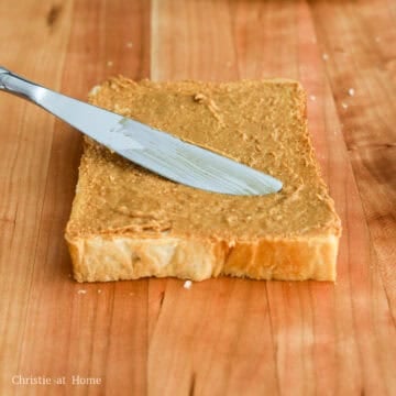 Two slices of white milk bread spread edge to edge with smooth peanut butter beside a plain slice of bread.