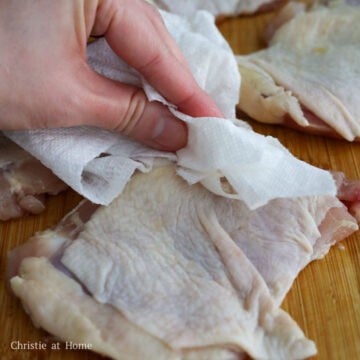 Patting chicken thighs dry with paper towels