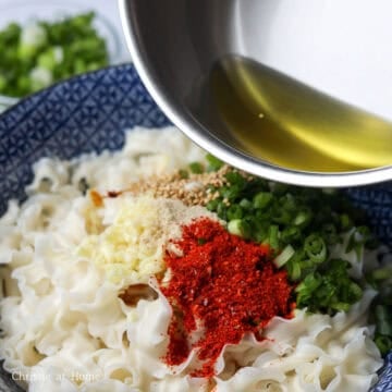Hot vegetable oil being poured over garlic, green onions, and chili flakes sitting on top of noodles to sizzle and infuse flavour.