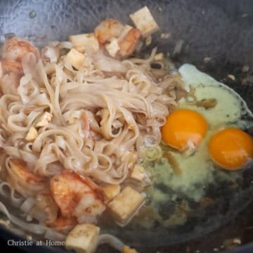 Add shrimp, then push everything to the side. Add remaining oil into the empty space of wok followed by eggs. Scramble them first and then mix in with noodles.