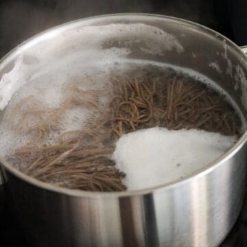 Buckwheat noodles cooking inside a pot of boiling water on a stovetop.