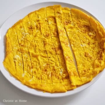 Heat 2 teaspoon of vegetable oil in a large pan on medium heat. Pour beaten eggs into the hot pan and swirl the eggs around the pan into a thin pancake. Flip the egg pancake over to cook through on the other side until golden. Transfer to a cutting board and slice egg pancake into ¾-inch wide strips. Set aside.