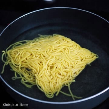 Fresh lo mein noodles being dropped into a large pan of boiling water to loosen up.