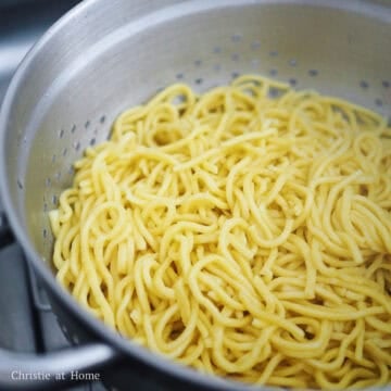 Emptying the hot lo mein noodles into a mesh strainer to drain the excess water.