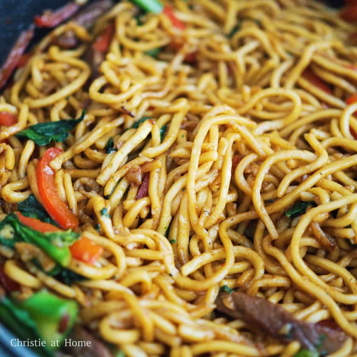 Tossing the fresh lo mein noodles, seared flank steak, bell peppers, gai lan, and caramelized sauce together in a large skillet.