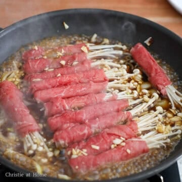 Beef enoki rolls simmering in broth over sliced onions