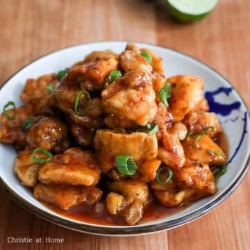 Crispy golden fried chicken pieces completely coated in a glossy, sticky red sweet chili glaze and topped with bright green chopped green onions.